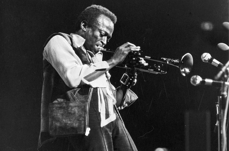 Miles Davis – Holding his trumpet, exuding quiet intensity.